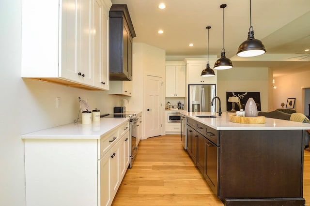 kitchen featuring stainless steel appliances, a sink, light wood-style floors, open floor plan, and light countertops