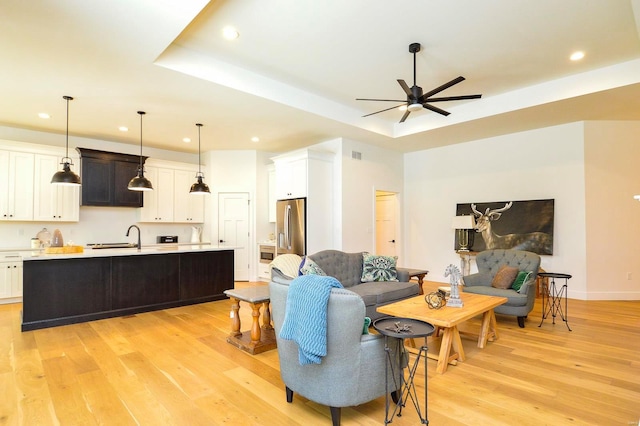 living area with light wood-style floors, ceiling fan, a tray ceiling, and recessed lighting