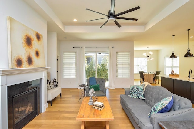 living room with a glass covered fireplace, a raised ceiling, light wood-style flooring, and baseboards