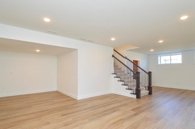 below grade area with light wood-type flooring, visible vents, stairway, and baseboards