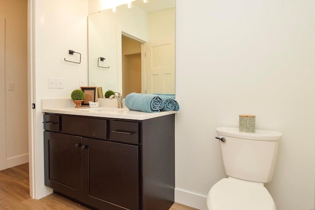 half bathroom with baseboards, vanity, toilet, and wood finished floors