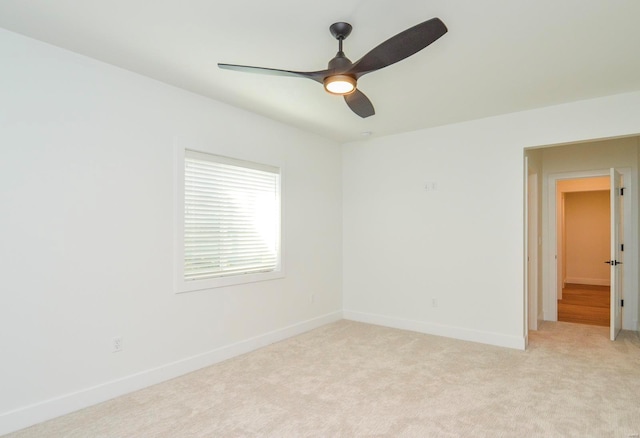 spare room featuring a ceiling fan, light colored carpet, and baseboards