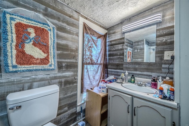 bathroom featuring wood walls, vanity, toilet, and a textured ceiling