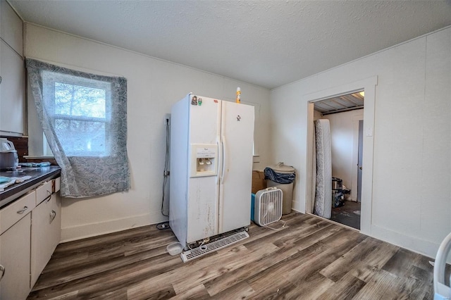 kitchen with white fridge with ice dispenser, dark countertops, a textured ceiling, and wood finished floors