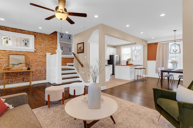 living room featuring light wood-type flooring, recessed lighting, brick wall, ceiling fan, and stairs