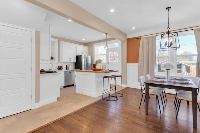 kitchen with light wood-type flooring, pendant lighting, a kitchen island, white cabinetry, and appliances with stainless steel finishes