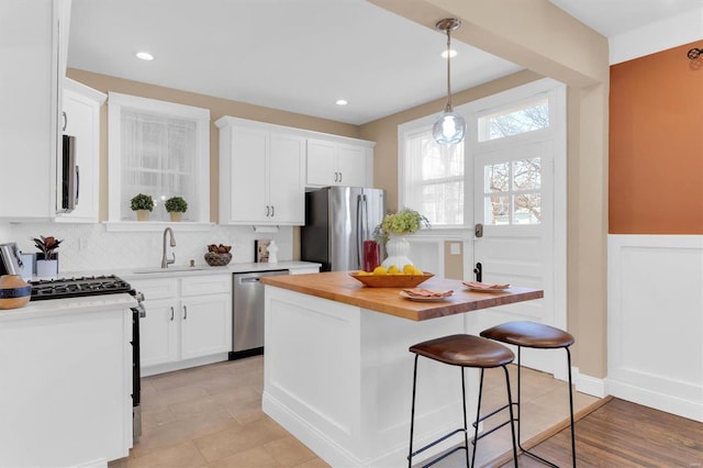 kitchen with a breakfast bar, a sink, wood counters, white cabinetry, and stainless steel appliances