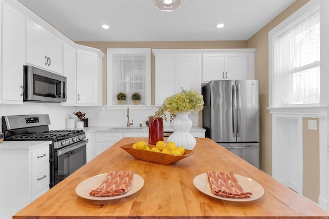 kitchen with butcher block countertops, a sink, a center island, appliances with stainless steel finishes, and white cabinets