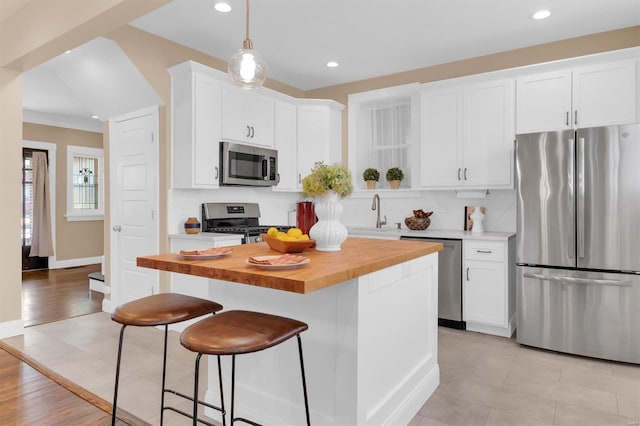 kitchen featuring stainless steel appliances, white cabinets, wood counters, a kitchen bar, and a center island