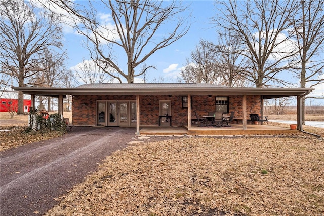 view of front facade featuring driveway, a patio, brick siding, and french doors