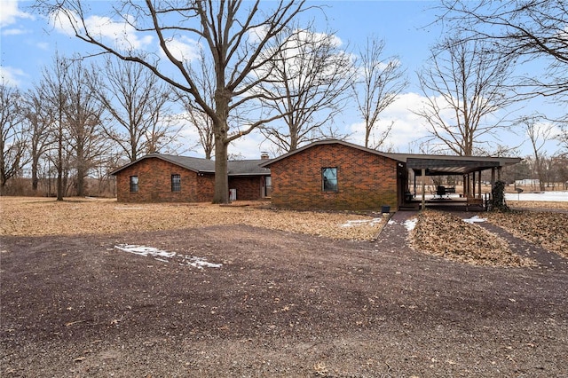 view of front facade featuring a carport, aphalt driveway, a chimney, and brick siding