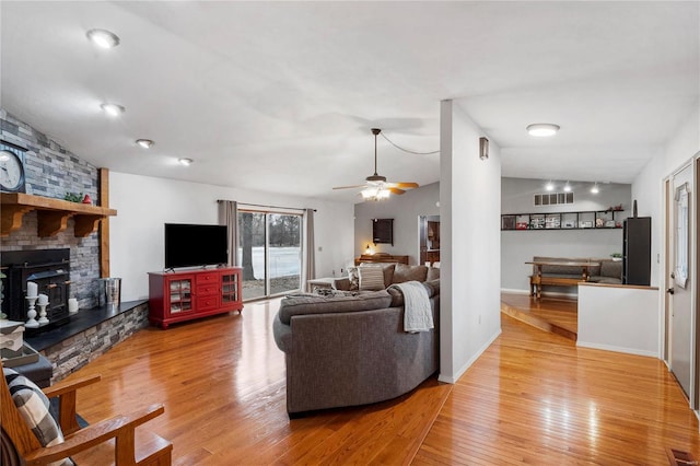 living area with lofted ceiling, a fireplace, visible vents, baseboards, and light wood-style floors