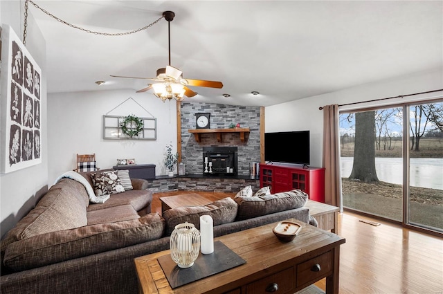 living room featuring ceiling fan, a large fireplace, wood finished floors, visible vents, and vaulted ceiling