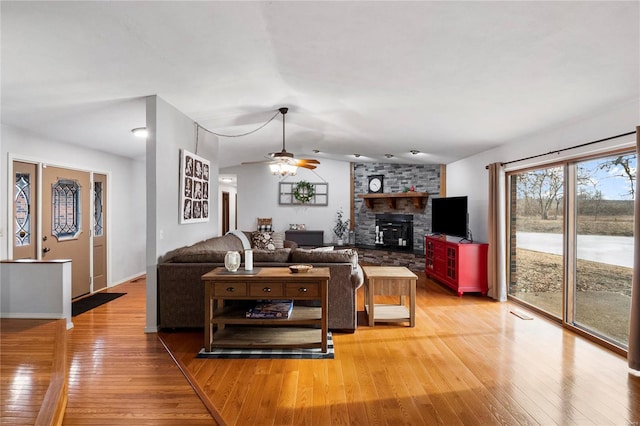 living area with light wood-style floors, ceiling fan, and a large fireplace