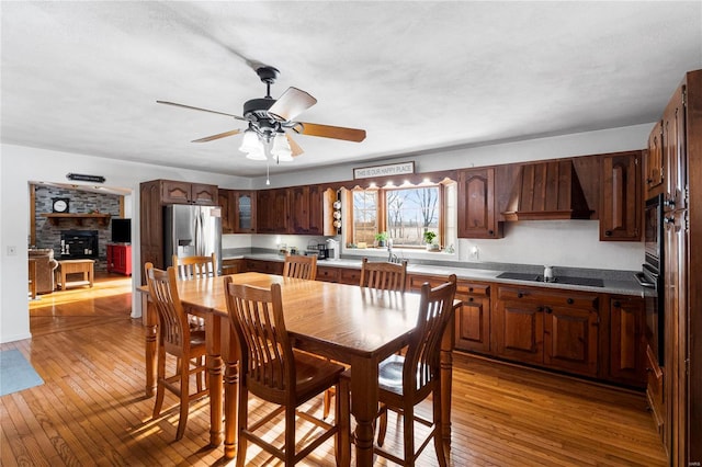 dining area with light wood-style flooring, a fireplace, and ceiling fan