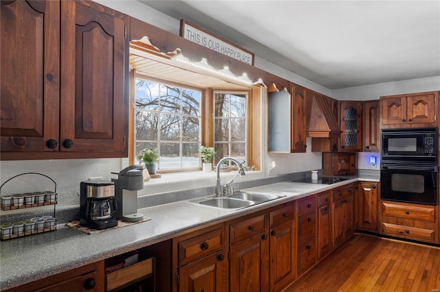 kitchen with light countertops, custom range hood, a sink, black appliances, and hardwood / wood-style floors