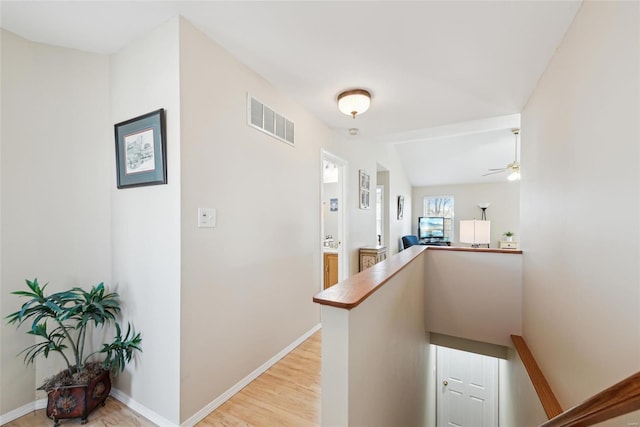 hallway featuring visible vents, light wood-style floors, vaulted ceiling, an upstairs landing, and baseboards