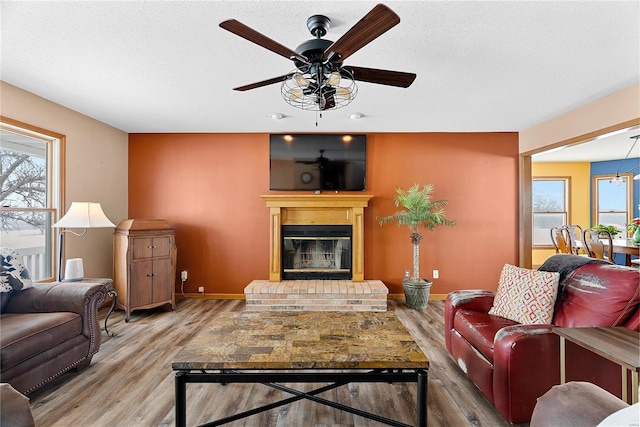 living room with wood finished floors, a brick fireplace, a healthy amount of sunlight, and a textured ceiling