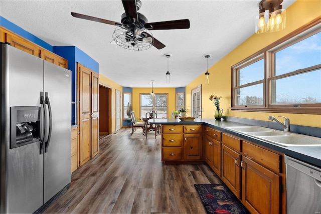 kitchen featuring brown cabinets, a sink, appliances with stainless steel finishes, a peninsula, and dark wood-style flooring