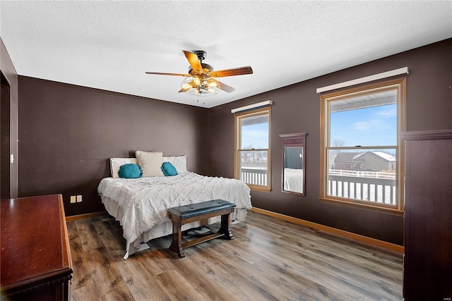 bedroom with ceiling fan, wood finished floors, baseboards, and a textured ceiling