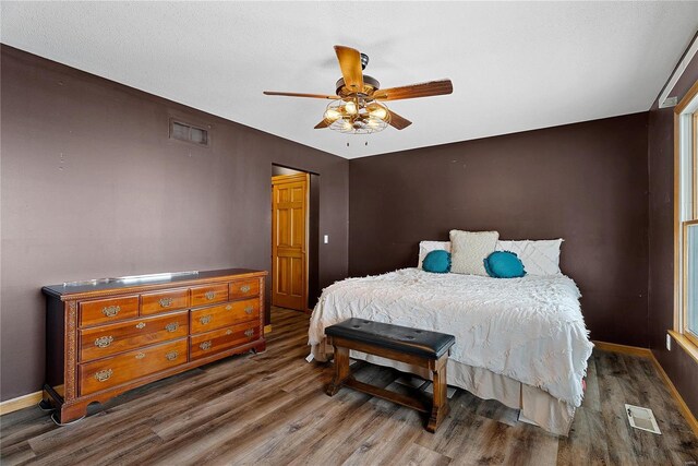 bedroom with ceiling fan, visible vents, baseboards, and wood finished floors