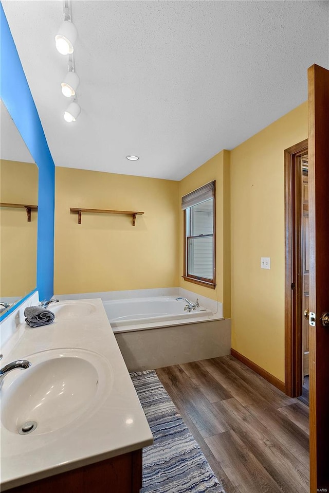 full bathroom featuring a bath, wood finished floors, a textured ceiling, and a sink