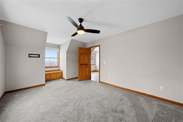 interior space with vaulted ceiling, light colored carpet, baseboards, and a textured ceiling