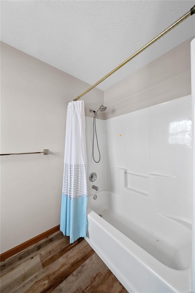 bathroom featuring a textured ceiling, shower / bath combo, baseboards, and wood finished floors