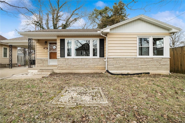 view of front of house featuring stone siding, a front lawn, fence, and an attached carport