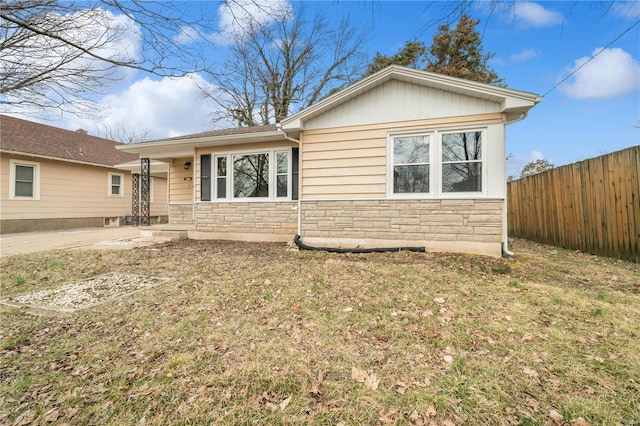 view of front facade featuring stone siding, fence, and a front lawn