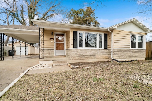 view of front of property featuring an attached carport, an outdoor structure, fence, driveway, and stone siding