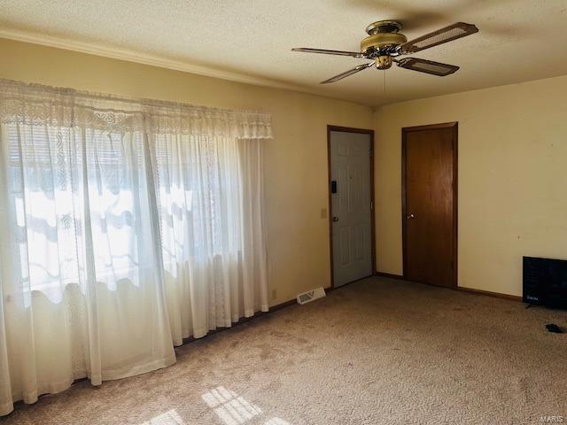 spare room featuring visible vents, light colored carpet, ceiling fan, and a textured ceiling