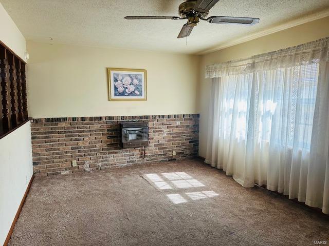 carpeted spare room featuring brick wall, ceiling fan, a fireplace, and a textured ceiling