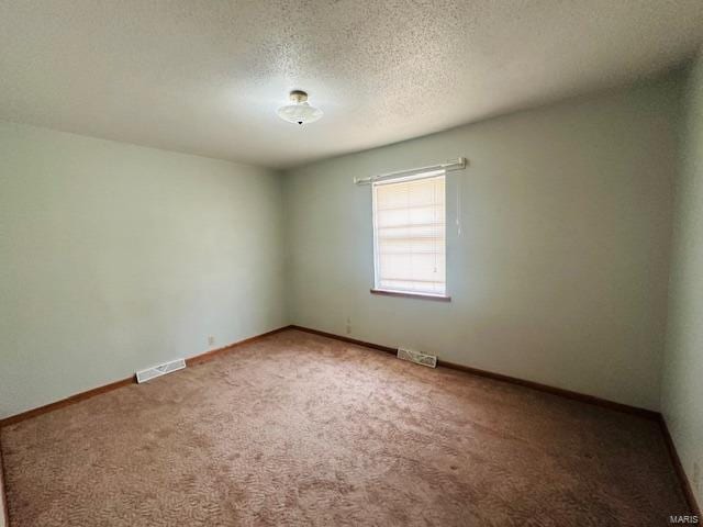 carpeted spare room with a textured ceiling, visible vents, and baseboards