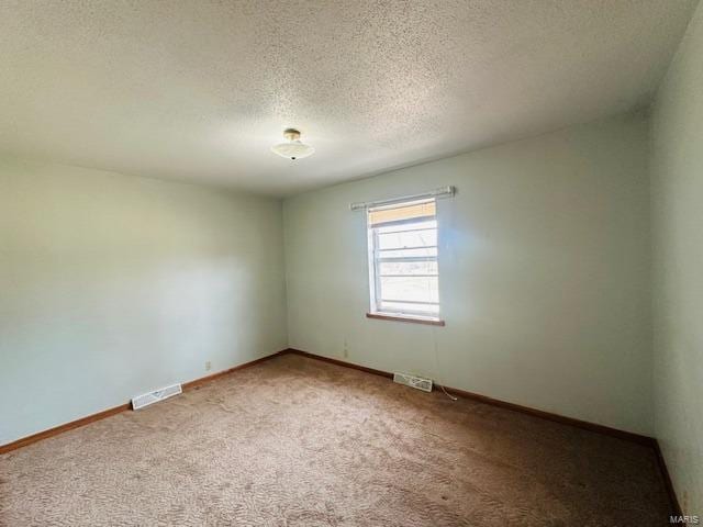 spare room featuring light colored carpet, visible vents, a textured ceiling, and baseboards