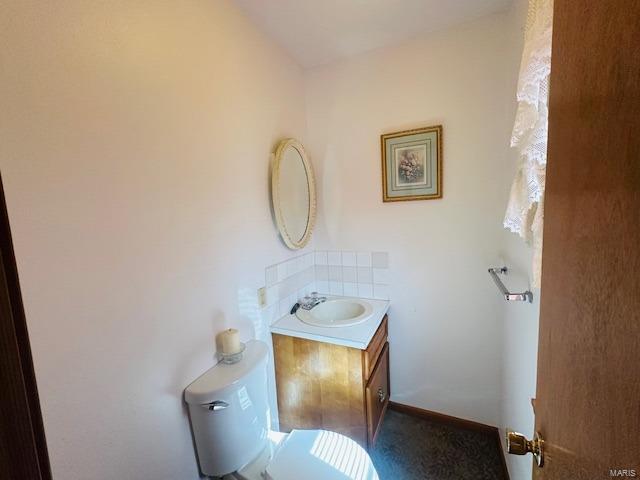 half bath featuring backsplash, baseboards, vanity, and toilet