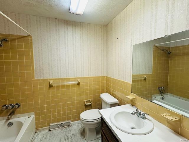 bathroom with visible vents, wainscoting, tiled shower / bath combo, a textured ceiling, and wallpapered walls