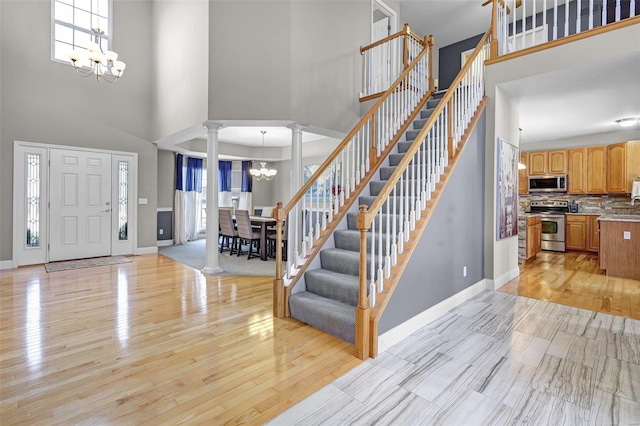 entryway with ornate columns, baseboards, light wood-style flooring, and an inviting chandelier