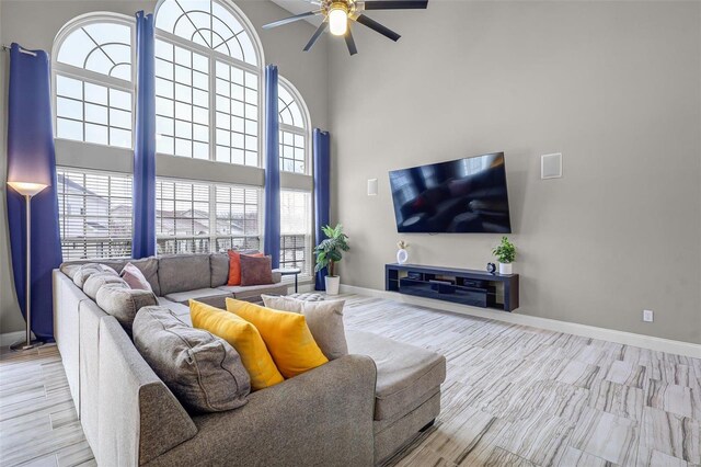 living area featuring a ceiling fan, a towering ceiling, baseboards, and wood finished floors