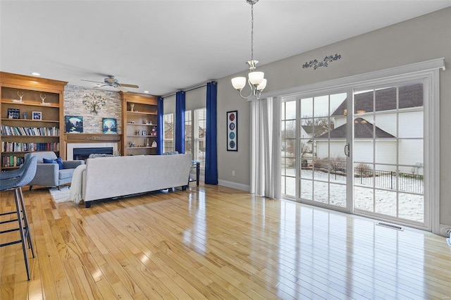 living area featuring a large fireplace, built in features, visible vents, light wood-style floors, and ceiling fan with notable chandelier