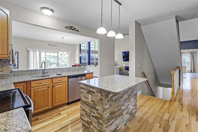 kitchen with light stone counters, light wood-type flooring, a sink, and stainless steel dishwasher