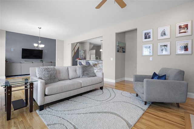 living area with light wood-type flooring, baseboards, and ceiling fan with notable chandelier