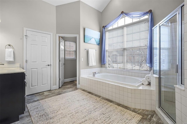 full bath featuring a stall shower, baseboards, wood finished floors, vanity, and a bath