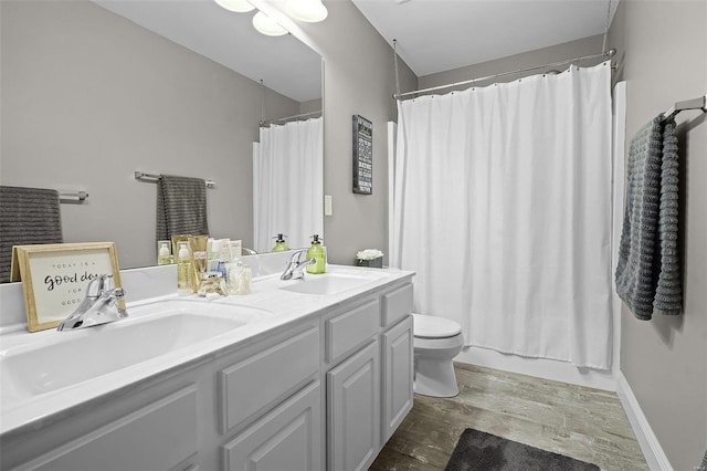 bathroom featuring toilet, double vanity, baseboards, and a sink