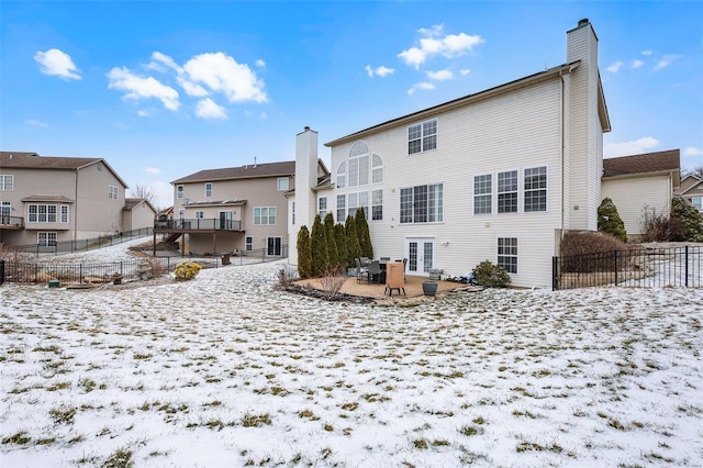 snow covered property with french doors, a chimney, and fence