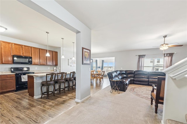 living area with a ceiling fan, carpet, baseboards, and wood finished floors