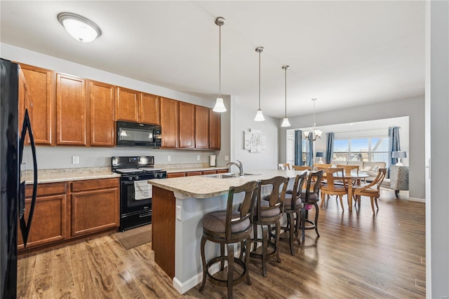 kitchen featuring a breakfast bar, light countertops, a sink, wood finished floors, and black appliances