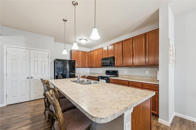 kitchen with light countertops, brown cabinetry, a sink, wood finished floors, and black appliances