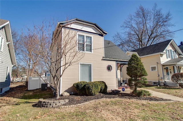 view of front of property featuring a shingled roof, fence, a front lawn, and central air condition unit