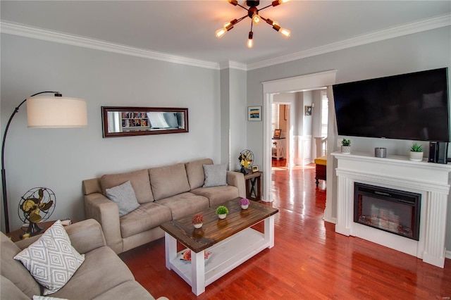 living area with ornamental molding, a glass covered fireplace, a notable chandelier, and wood finished floors